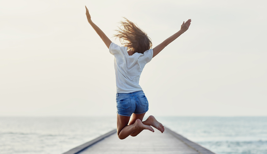 A woman jumping with joy on a dock leading out to the ocean